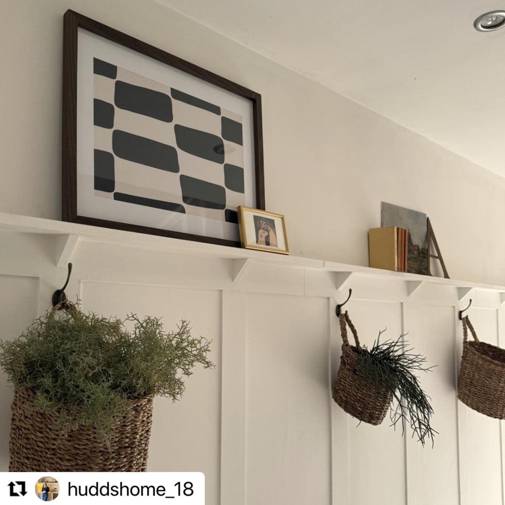 Made-to-measure shaker panelling in a bright hallway styled with wall hooks, woven baskets, trailing plants and a long display shelf above.