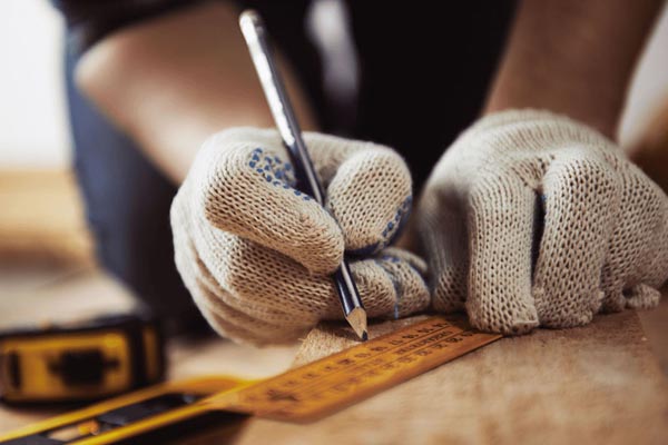 Hands holding a pencil marking wood with a ruler