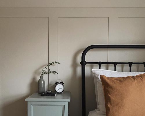 Beige wall panelling with a black metal bed and alarm clock