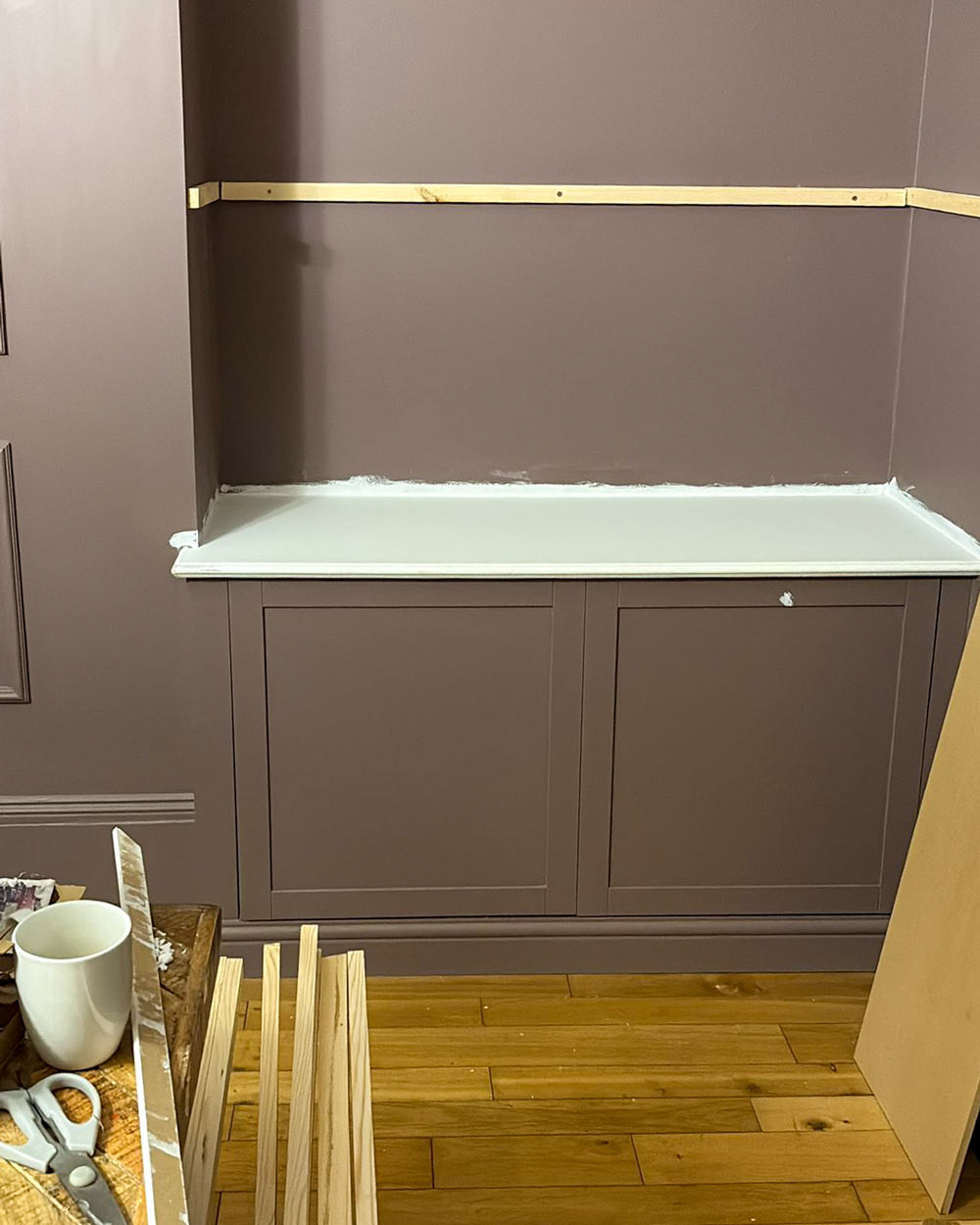 Mid-build stage of IKEA Besta built-in, showing MDF top panel fitted and timber battens attached to the wall for shelving support.